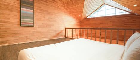 Une chambre avec un plafond en bois, un lit, une fenêtre et une œuvre d’art encadrée accrochée au mur.