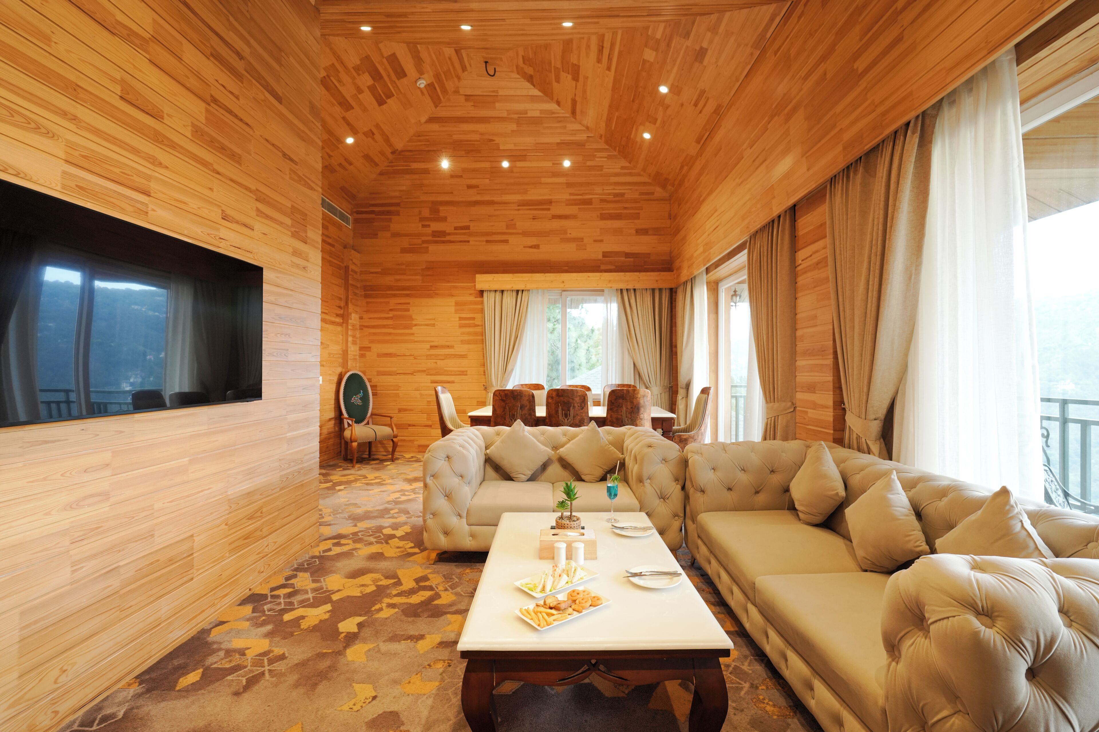 A wooden-paneled room with a sofa, a dining table with a cake, and a TV on the wall.