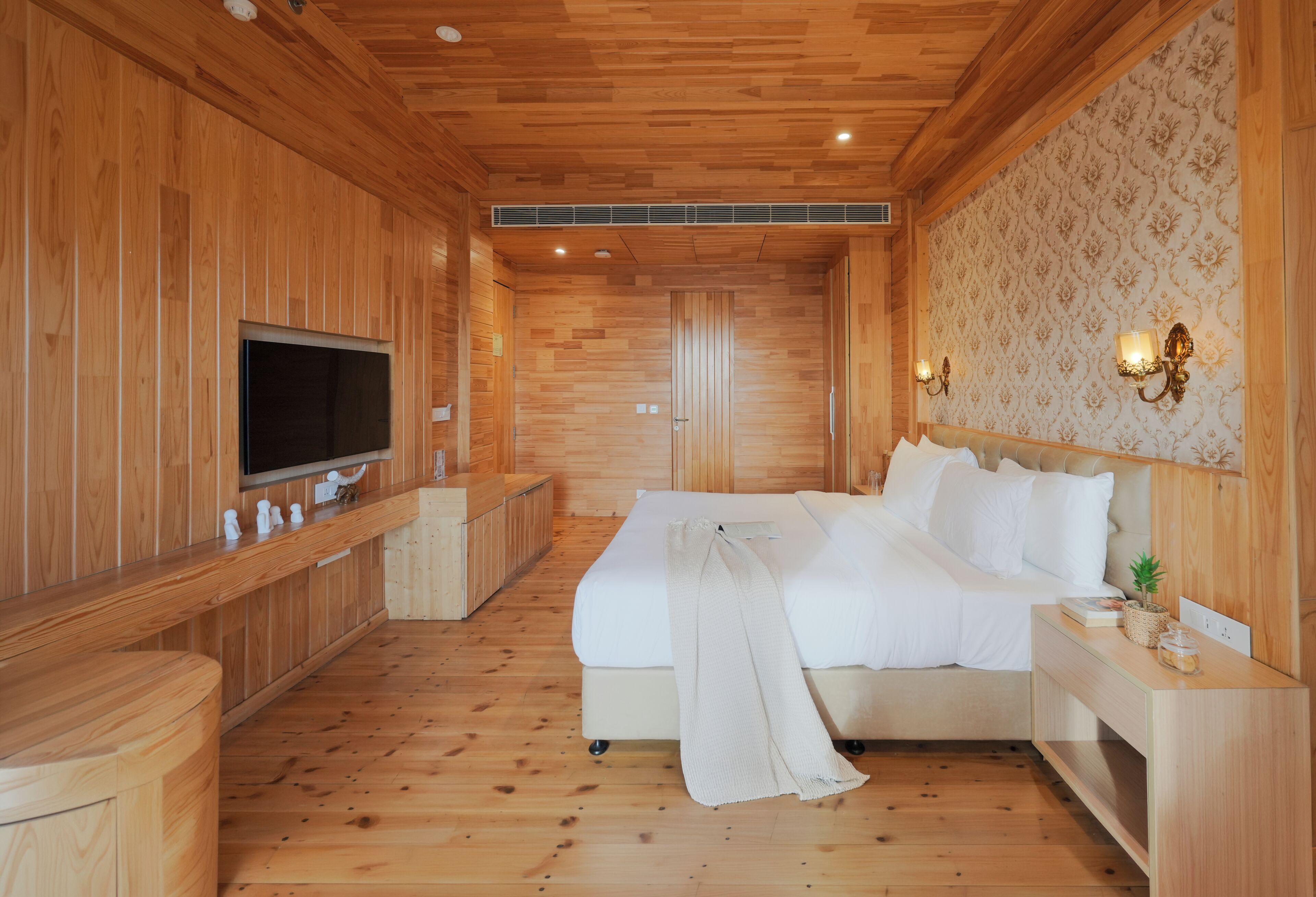 A wooden-paneled room with a bed, a TV, and a wall-mounted light fixture.