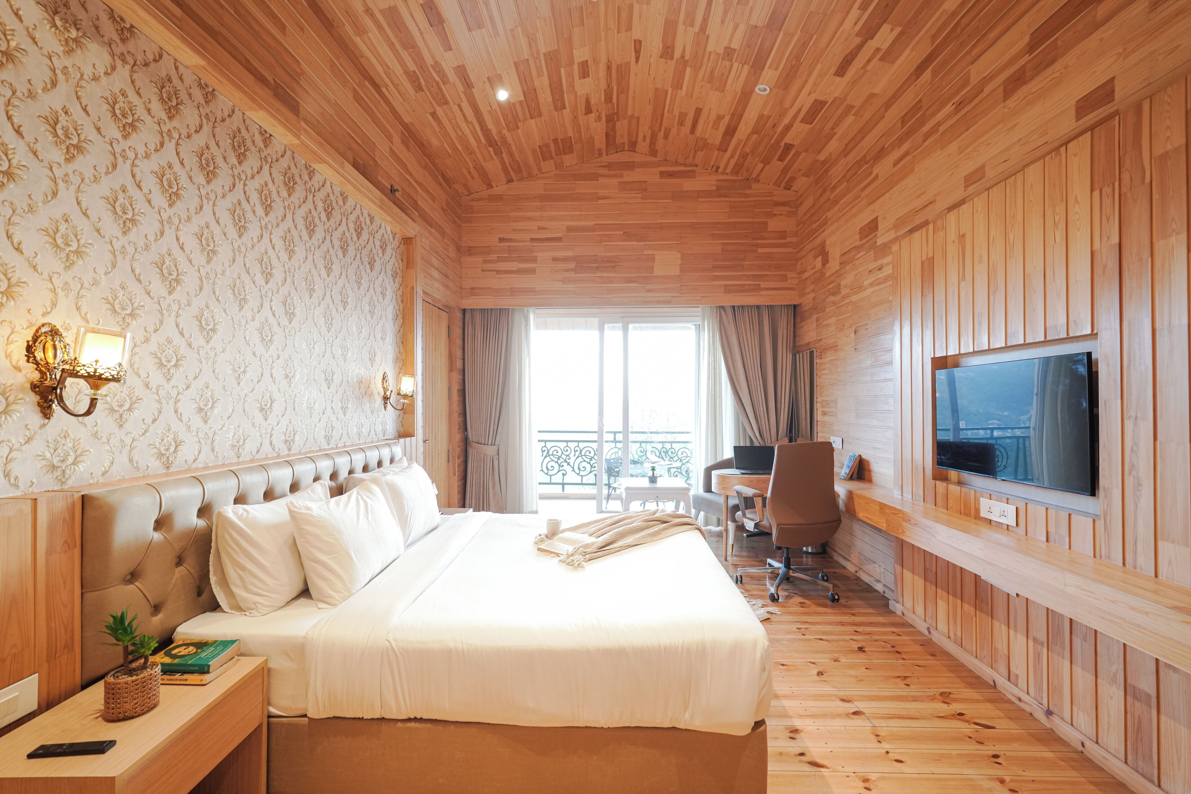 Habitación de hotel con techo de madera, cama con ropa de cama blanca, televisor en la pared y balcón con vistas.