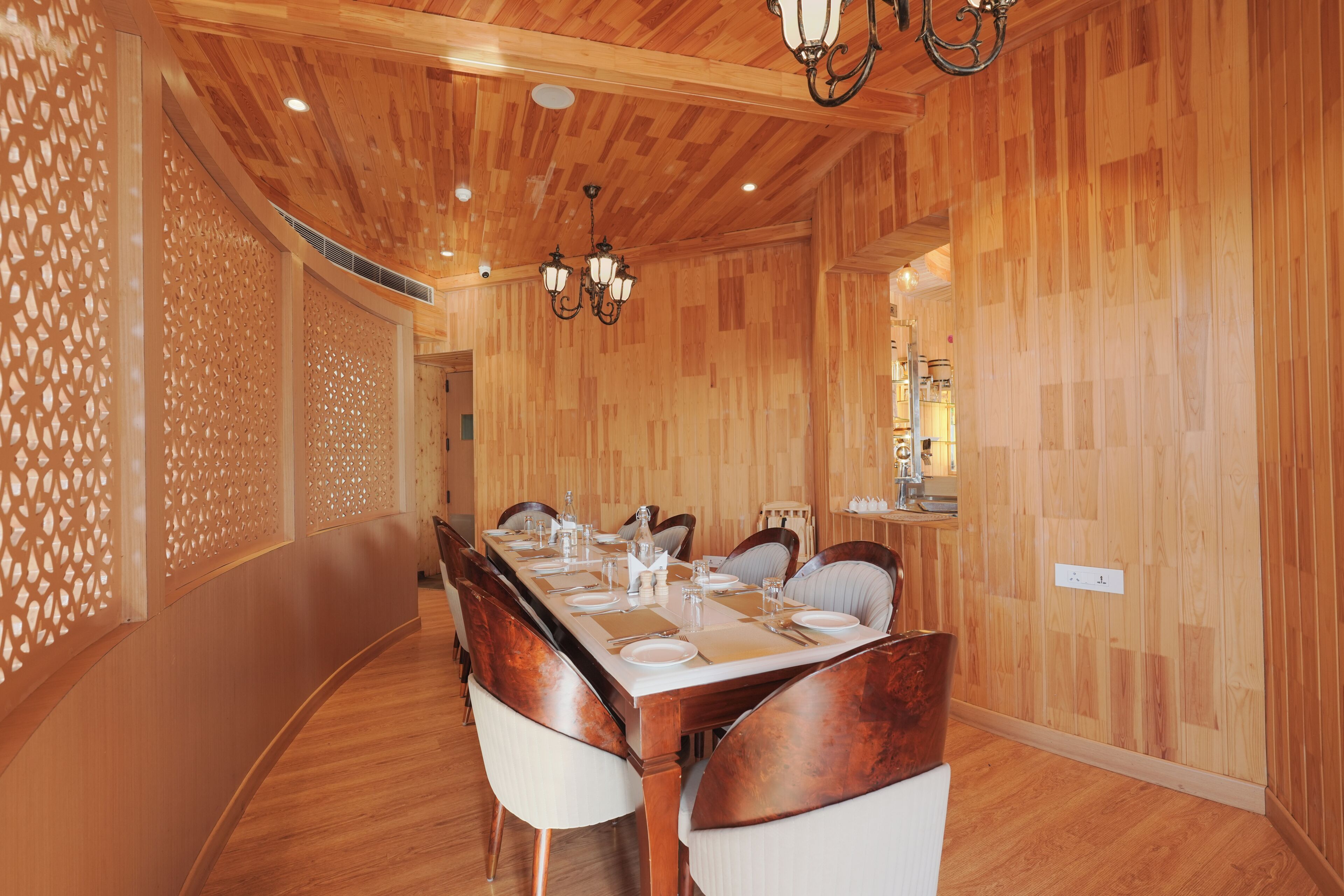 Een eethoek met een lange houten tafel voor zes personen, omringd door stoelen, met een houten plafond en muren, en een decoratieve lamp.