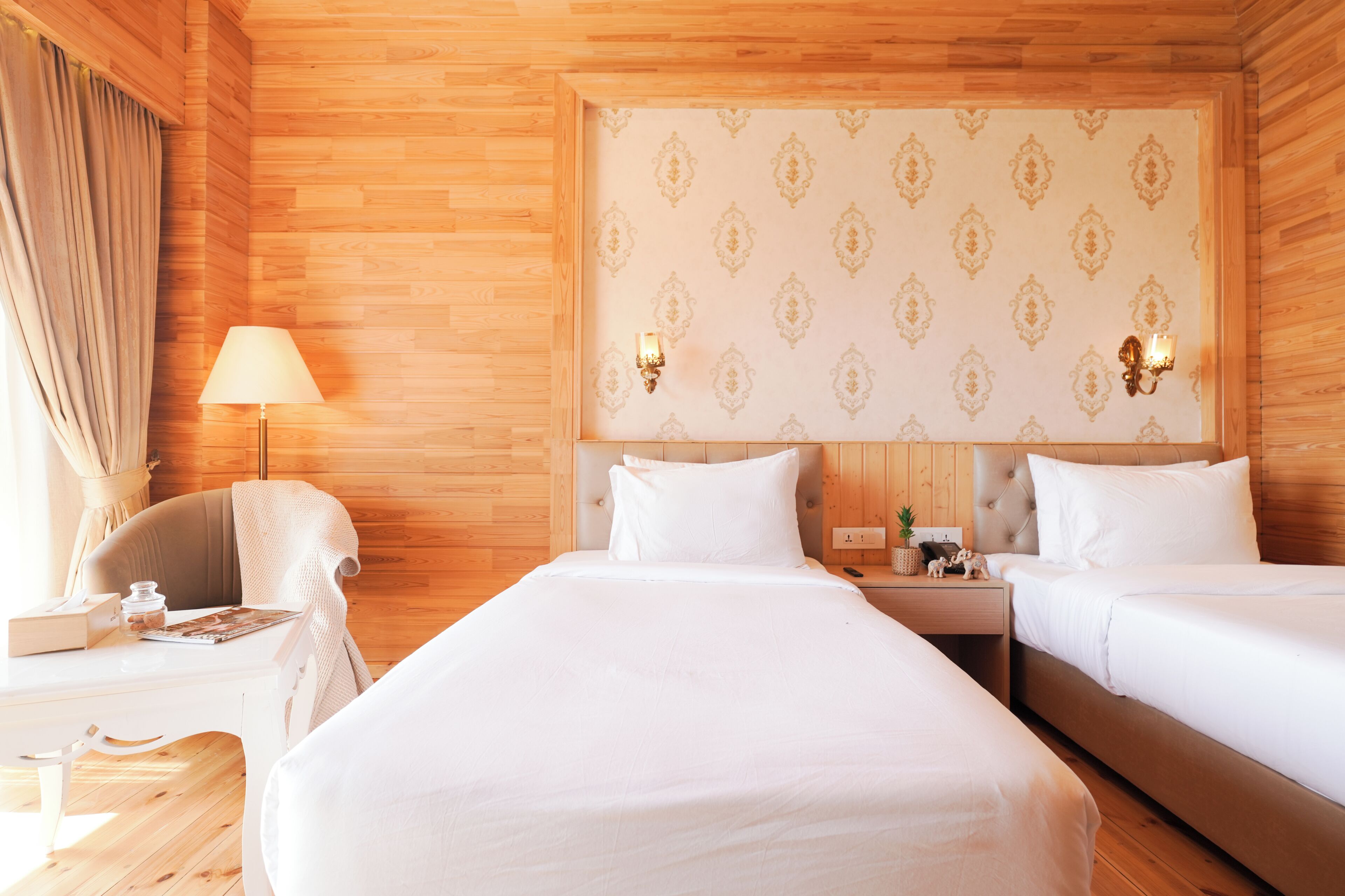 A hotel room with two beds, a nightstand, a lamp, and a chair.