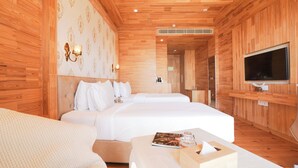 A hotel room with wooden paneling, a large bed, a TV, and a bedside table with a magazine. - Treetop by Eight Continents Royalpine HP (Kasauli)
