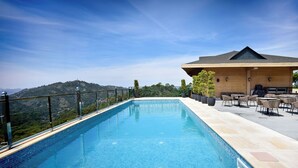 A swimming pool with a view of a mountainous landscape, a wooden building with outdoor seating, and a fenced area. - Treetop by Eight Continents Royalpine HP (Kasauli)