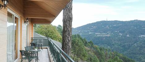 A balcony with a view of a mountainous landscape, a wooden ceiling, and outdoor furniture.