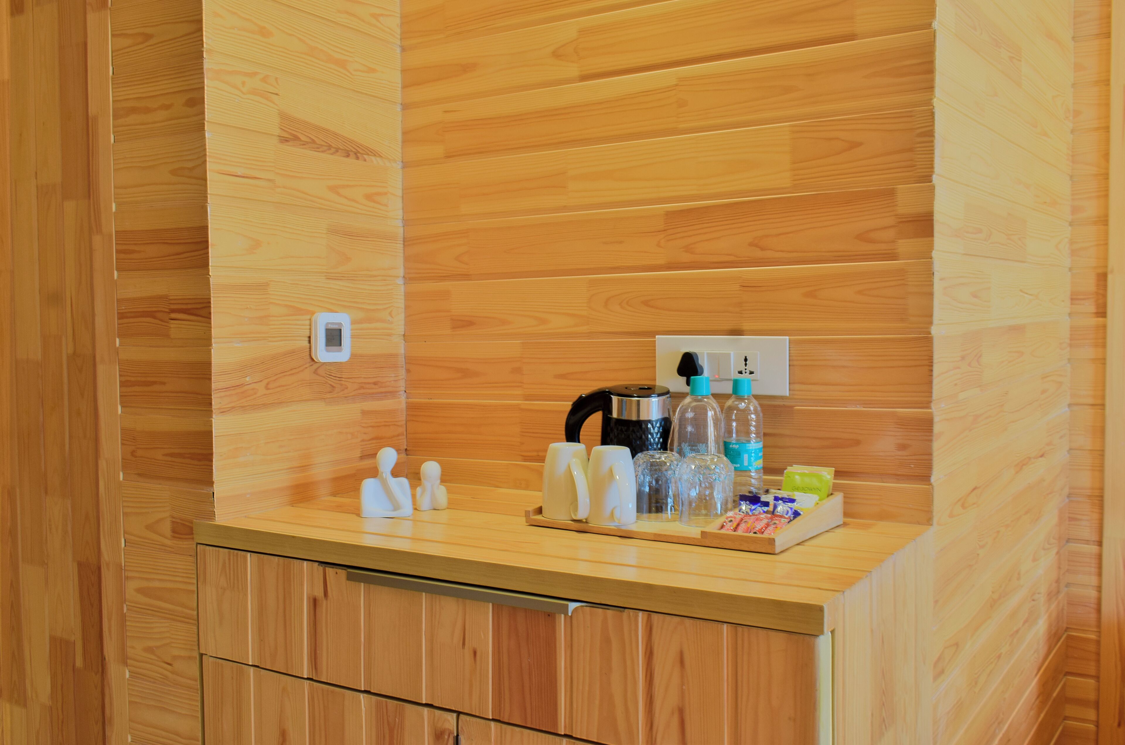 Pared de madera con mostrador integrado, hervidor, varias botellas y tazas.