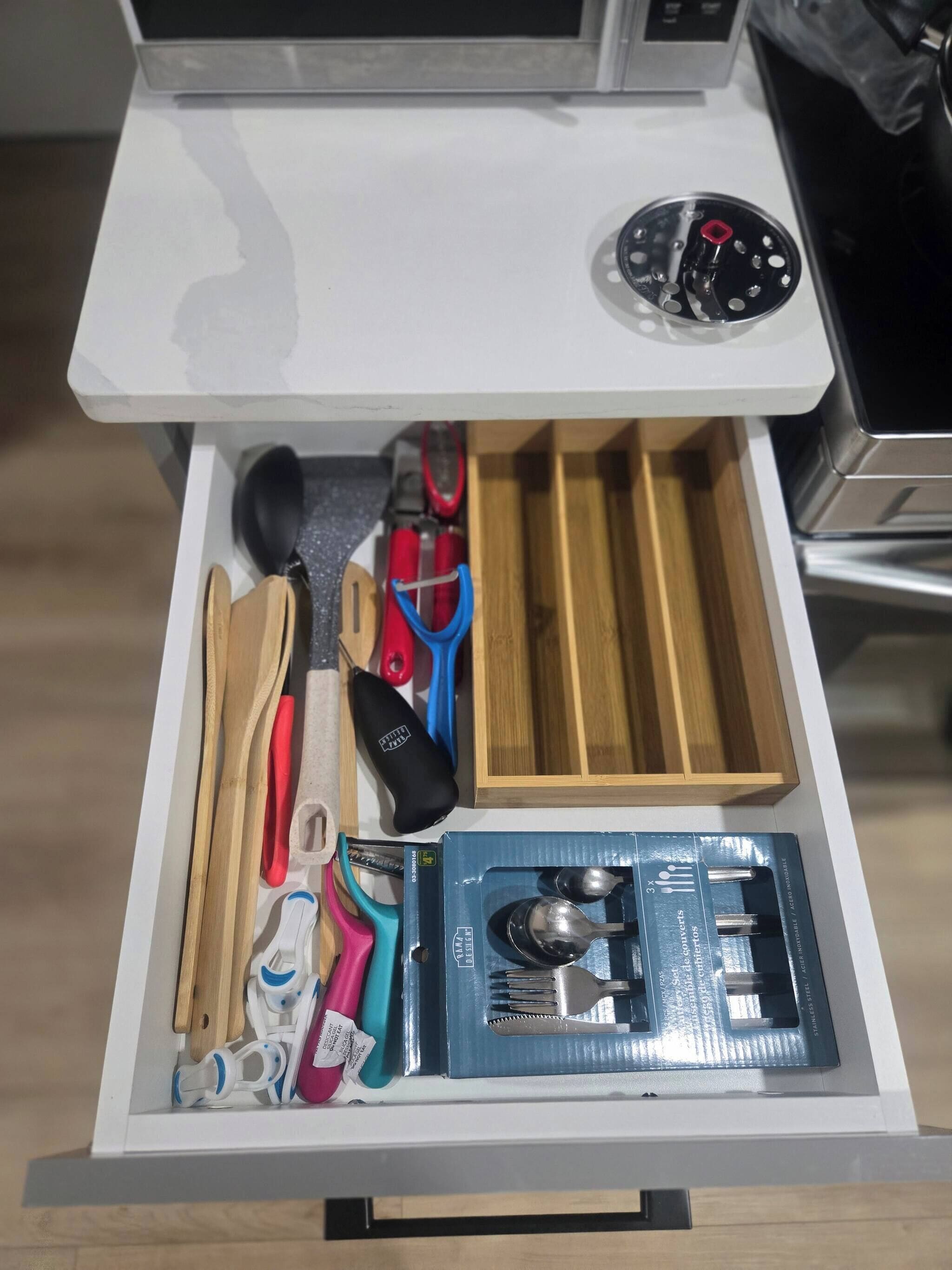 A drawer with various kitchen utensils, including a wooden spoon, a pair of scissors, and a set of tongs.