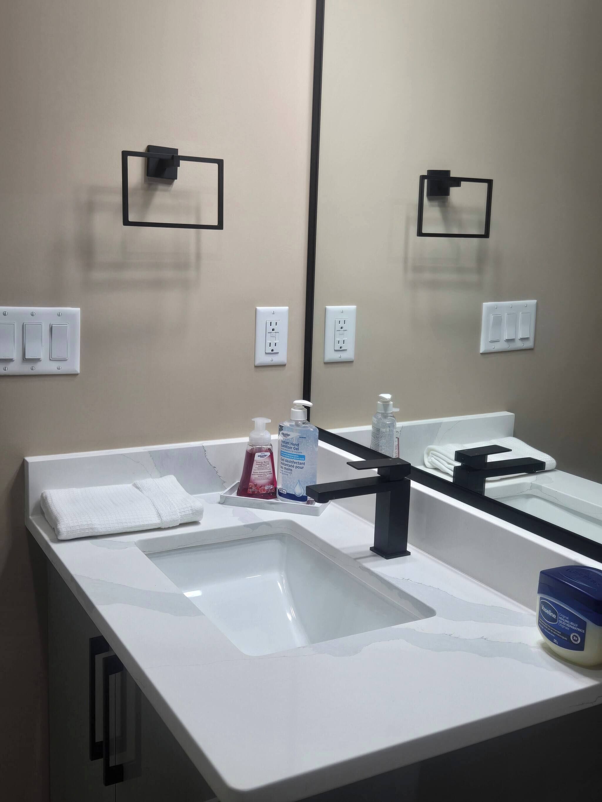 A bathroom with a white sink, a mirror, and two electrical outlets on the wall.