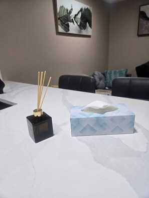 Une pièce avec une table en marbre blanc, un objet noir de forme carrée avec des baguettes, une boîte de mouchoirs et un canapé avec des coussins.
