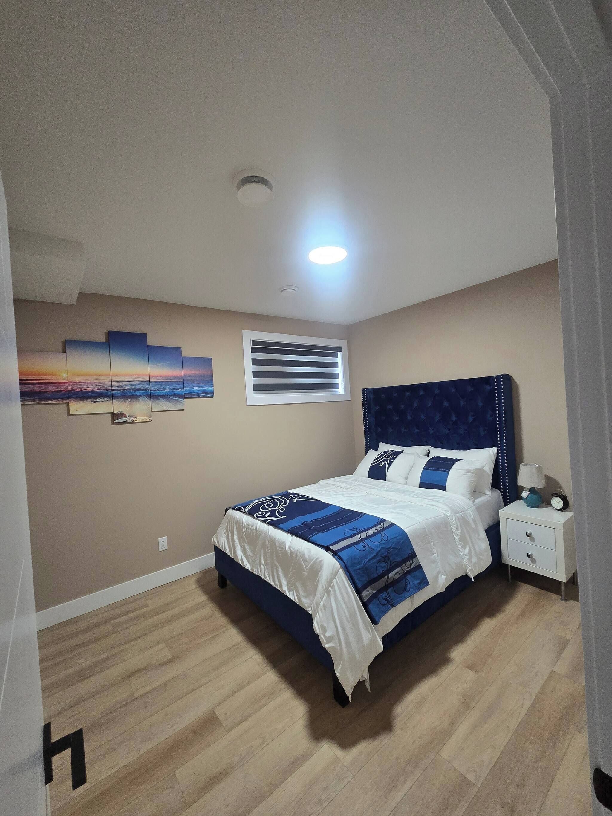 A bedroom with a bed, nightstand, wall art, and a window with blinds.