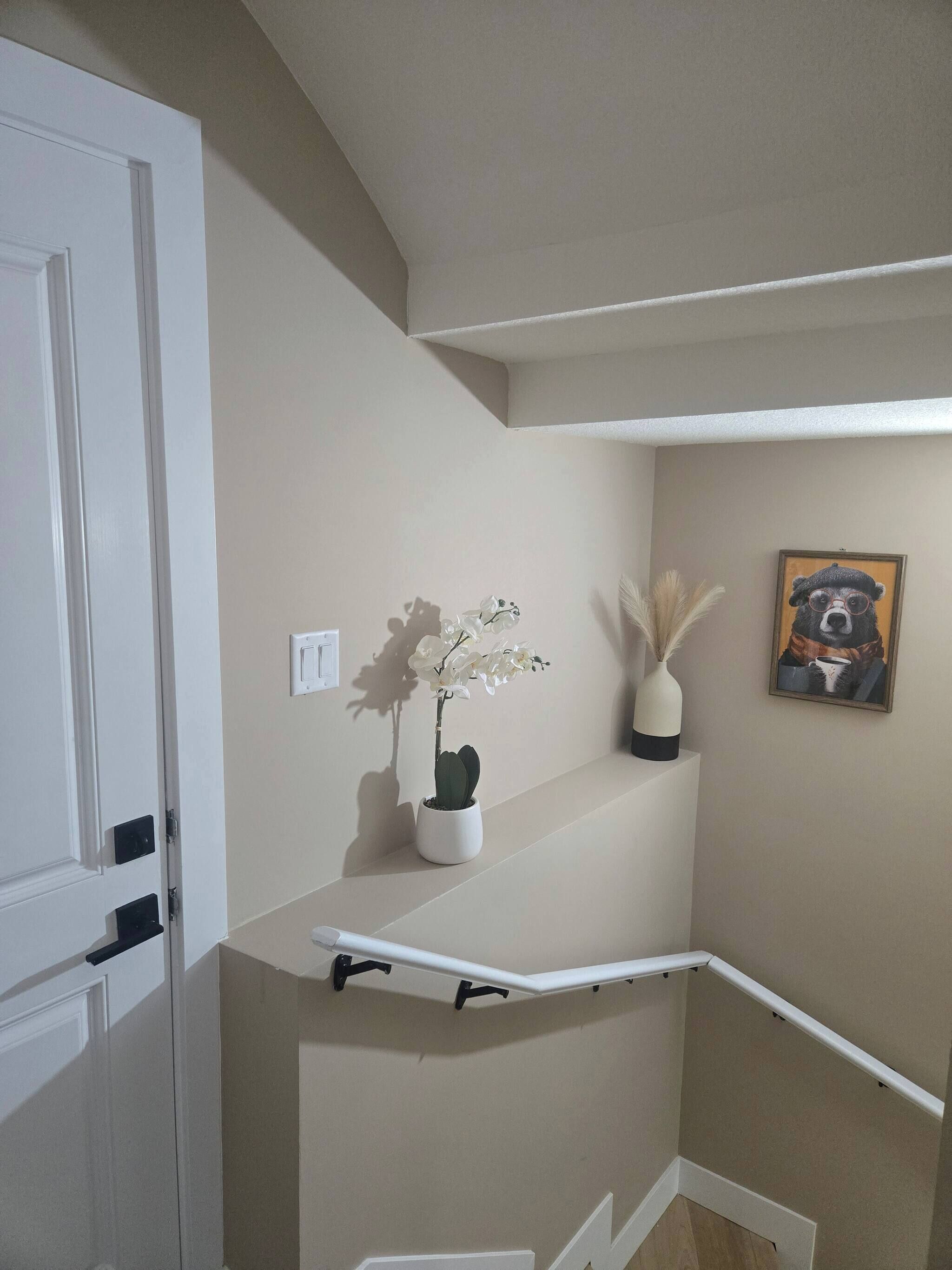 Uma escadaria com corrimão branco, uma orquídea em vaso e uma obra de arte emoldurada na parede.