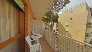 Ein Balkon mit Tisch und Stühlen, ein weißer Zaun und ein Gebäude mit sandfarbener Fassade.