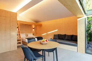 Ein modernes Interieur mit einer Holzverkleidung, einem Bett, einem Sofa, einem Esstisch mit Stühlen und einer Obstschale.