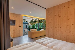 Ein modernes Schlafzimmer mit einer Couch, zwei Betten, Holzwänden und Blick ins Grüne.