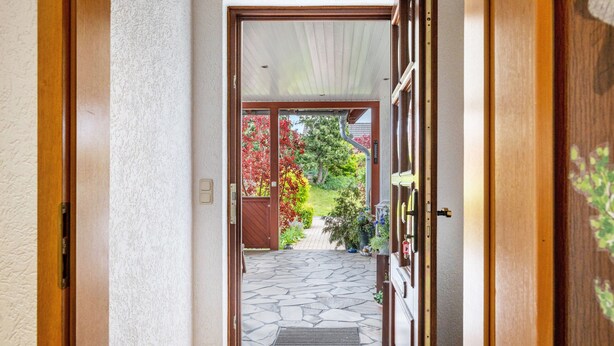 A hallway leading to a garden with a stone pathway and wooden doors.