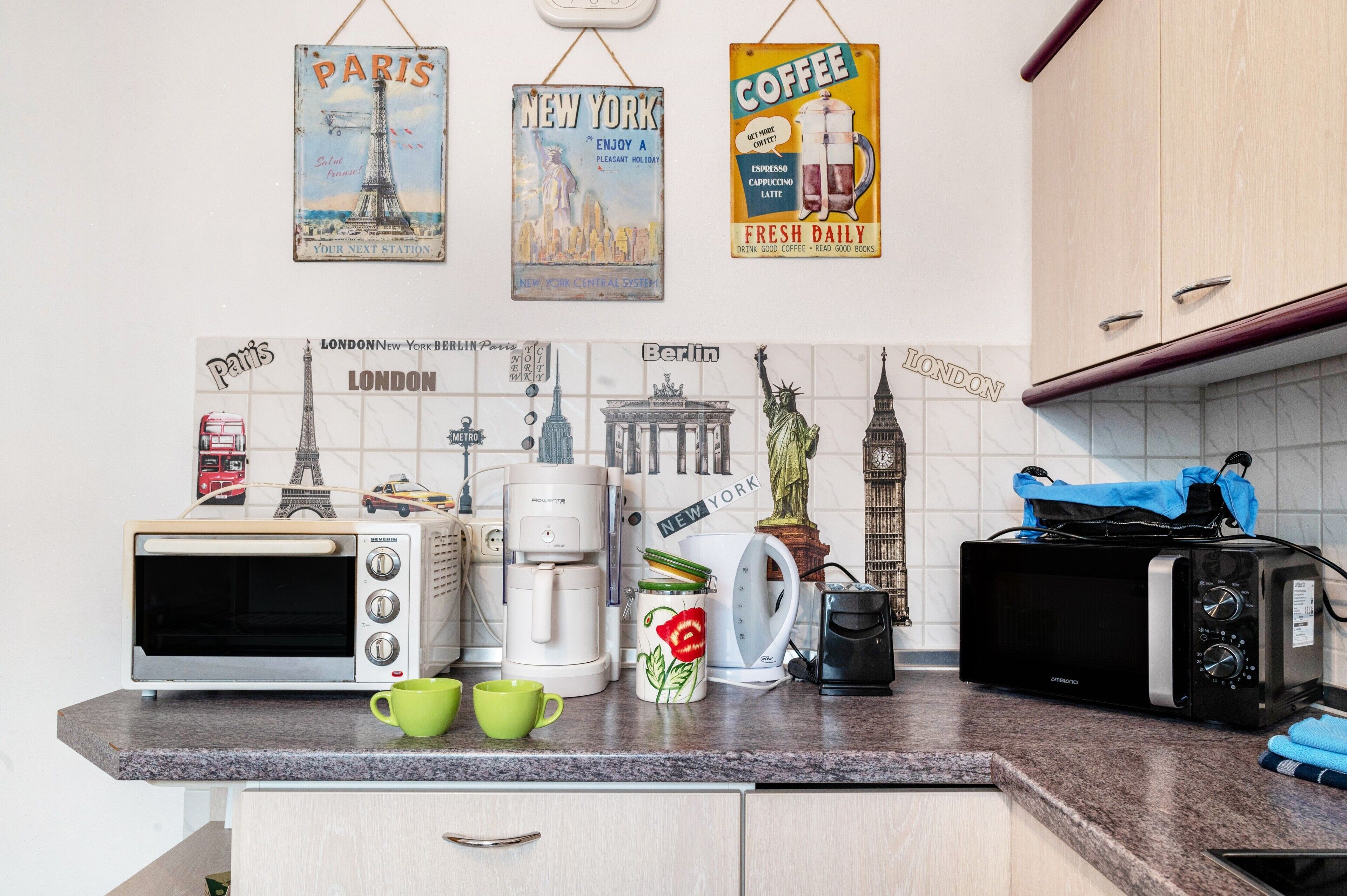 A kitchen with a toaster, coffee maker, and a kettle. There are mugs on the counter.