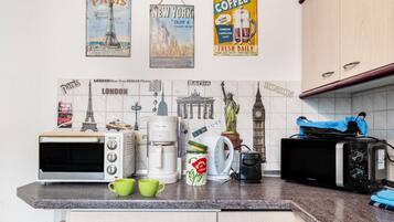 A kitchen with a toaster, coffee maker, and a kettle. There are mugs on the counter.