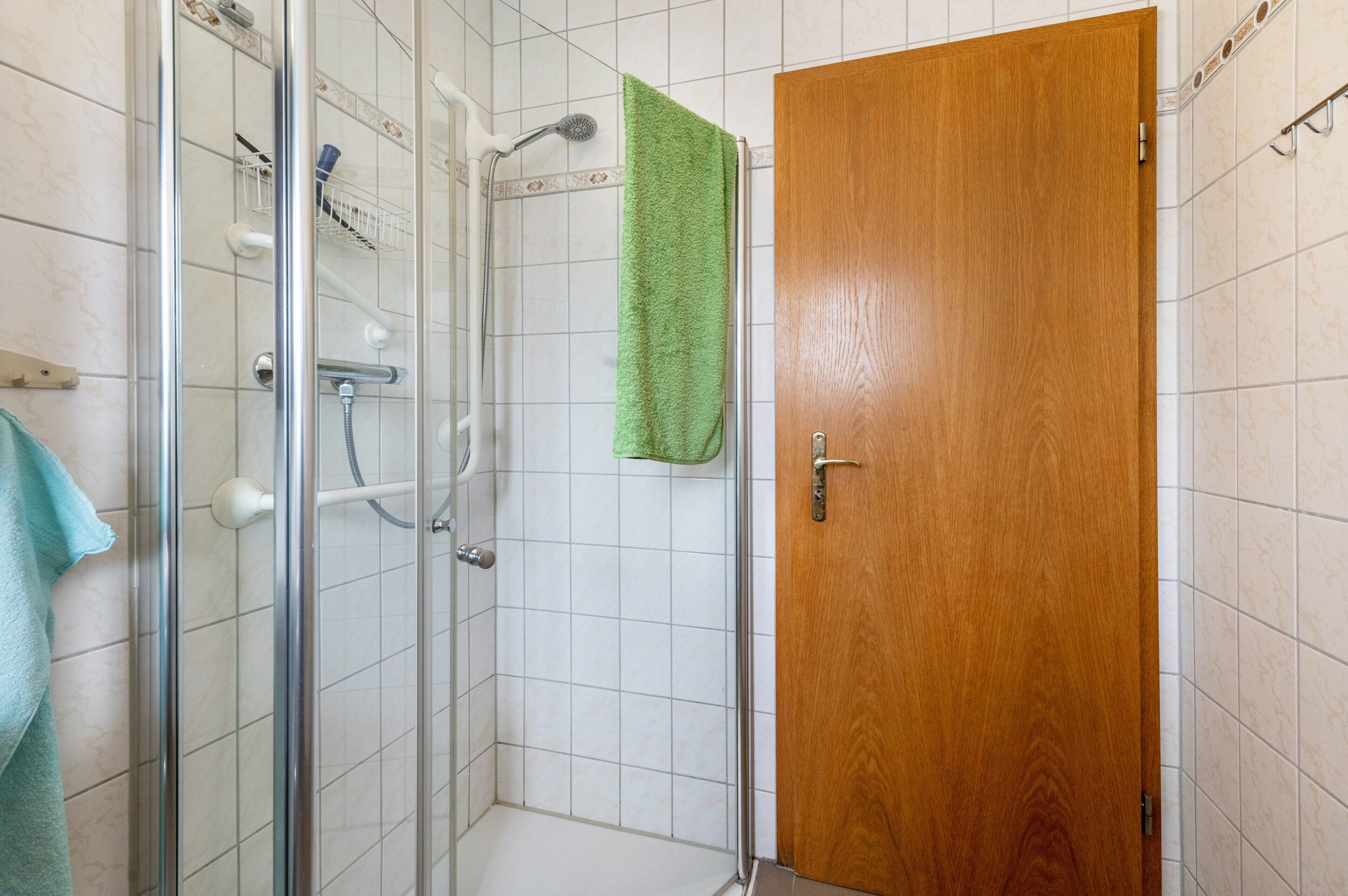 Eine Dusche mit Glastür, eine Holztür und ein grünes Handtuch an der Wand.