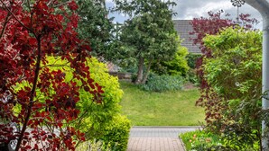 A garden pathway leading to a building with a brick entrance, surrounded by various shrubs and trees.