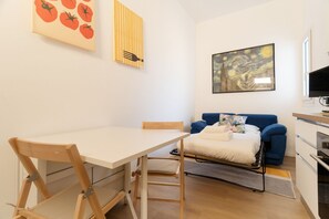 A compact living space with a dining table, a sofa, a bed, and a kitchen area.