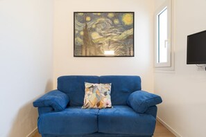 A blue sofa with a floral pillow, a framed artwork above it, and a television on the wall. - Cozy 40m2 apartment, perfect for 3 people, located on the ground floor of a building.The accommodation is located in Gorla, a historic district of Milan, located in Municipio 2 along Viale Monza, known as the Little Paris for the enchanting atmosphere  (Milan)