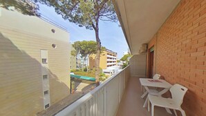 Ein Balkon mit weißen Stühlen und einem Tisch, mit Blick auf eine Straße mit Gebäuden und einem Baum.