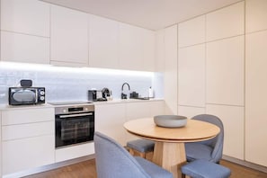 Eine moderne Küche mit weißen Schränken, einer Mikrowelle, einem Backofen, einer Kaffeemaschine und einem runden Tisch mit Stühlen.