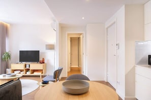 Ein modernes Wohnzimmer mit Flachbildfernseher, einer Holz-Unterhaltungseinheit, einem Esstisch mit Schüssel und einer Couch.