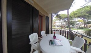 A round table with white chairs on a balcony, a closed dark wooden door, and a view of buildings and trees. - Family-friendly stay in Lignano (Lignano Sabbiadoro)