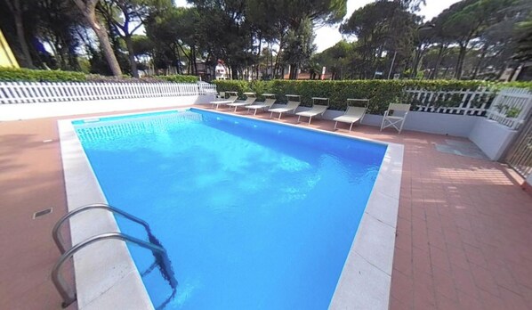 Une piscine rectangulaire bordée de blanc, entourée d’une allée pavée et d’une clôture blanche.