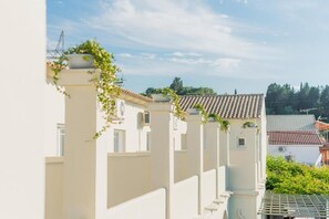 Una hilera de edificios blancos con tejados de cerámica, cielo despejado y vegetación al fondo.