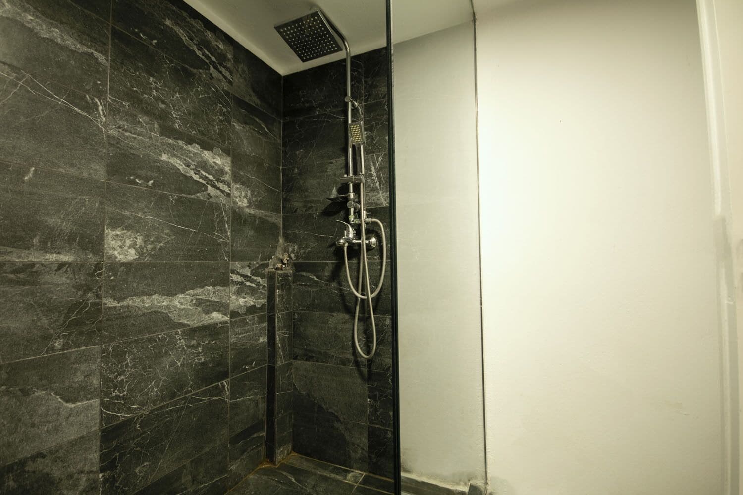 A shower with a handheld showerhead and a wall-mounted faucet, set against dark marble tiles.
