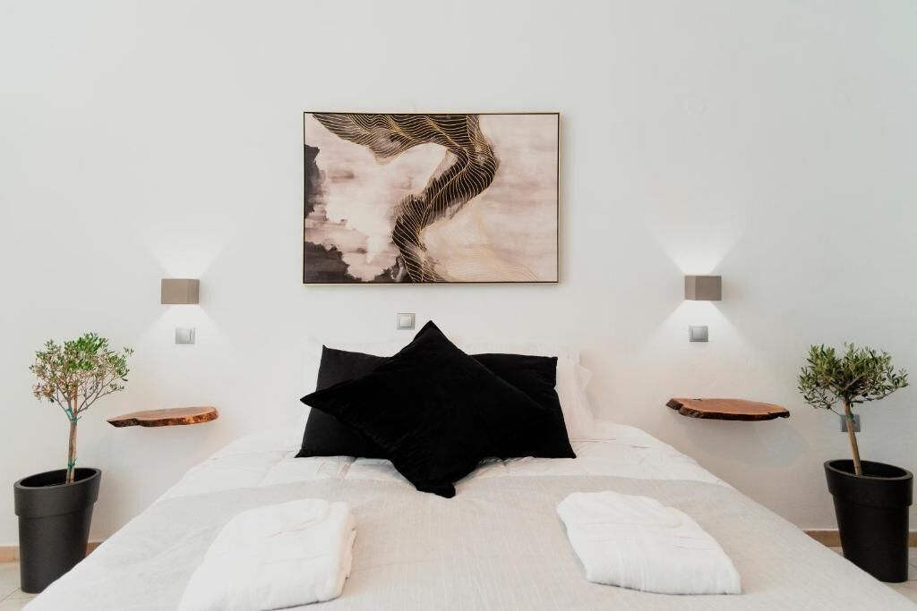 A bedroom with a bed, a wall-mounted abstract painting, bedside tables with plants, and wall-mounted lights.