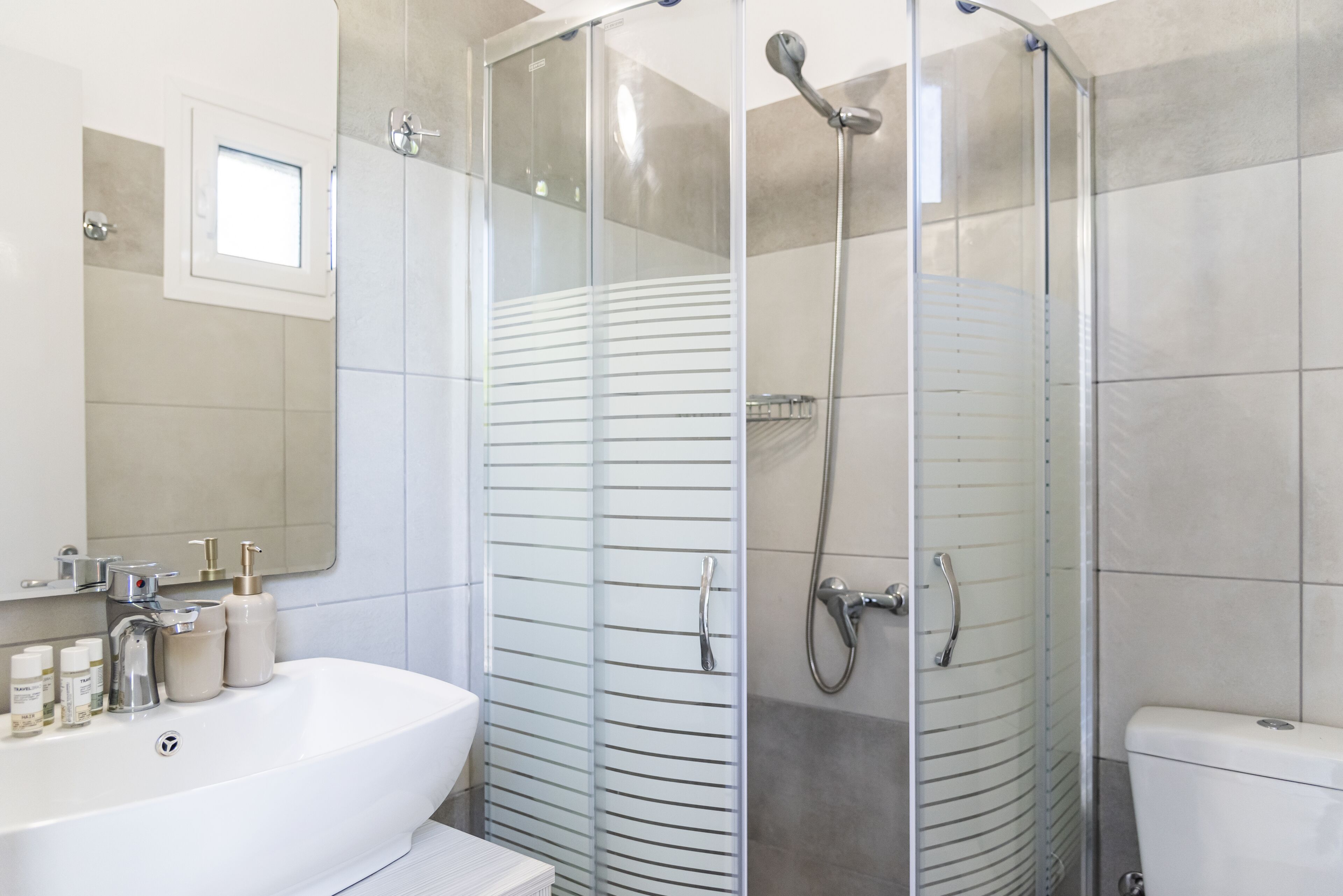 A modern bathroom with a glass-enclosed shower, a white sink with toiletries, and a toilet.