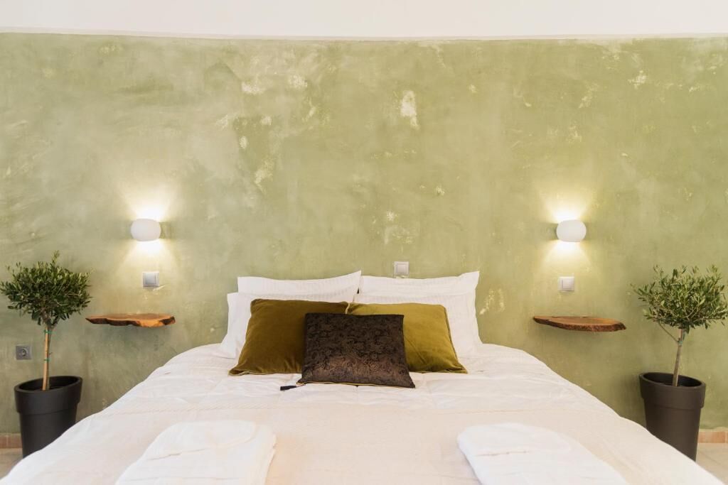 A bed with white linens, a dark brown pillow, and two bedside tables with wall-mounted lights.