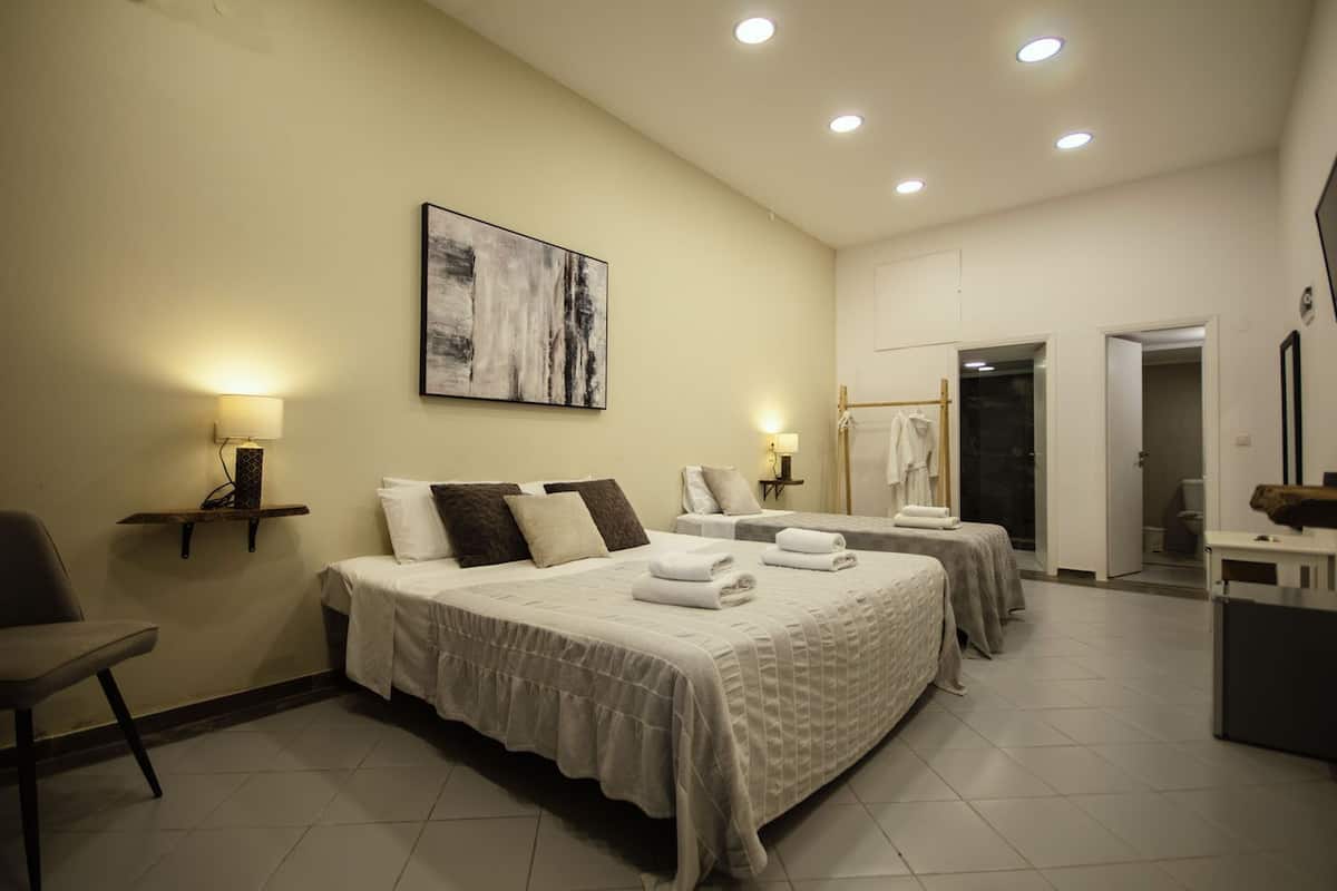 A hotel room with two beds, a chair, a desk, a bathroom, and a painting on the wall.