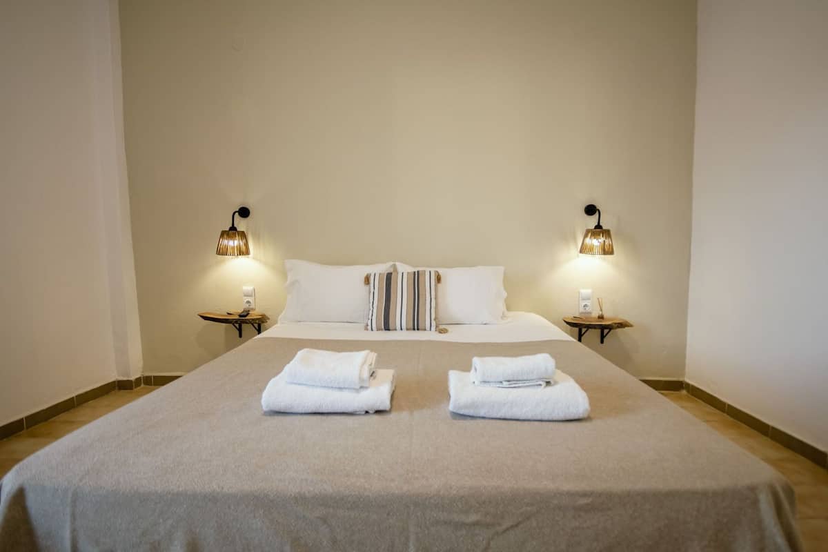 A neatly made bed with two pillows, two bedside tables with lamps, and two folded towels on the bed.