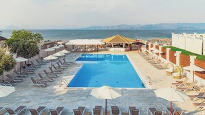 A pool area with lounge chairs and umbrellas, a bar, and a view of the sea. - Ionian Blue Beach - Adults Only (Corfu)