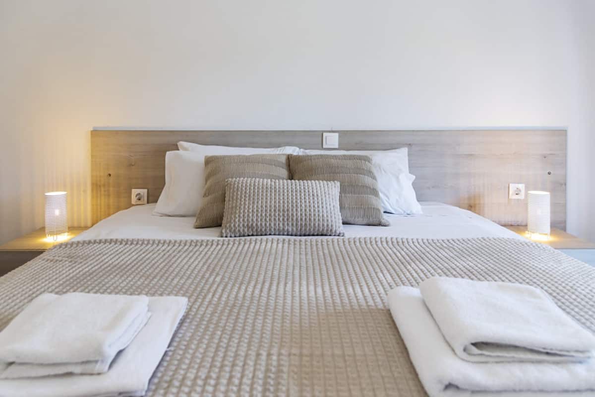 A neatly made bed with a patterned bedspread, two pillows, and two folded towels on a wooden headboard.