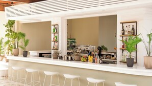 A bar area with white bar stools, shelves with bottles, and potted plants. - Ionian Blue Beach - Adults Only (Corfu)