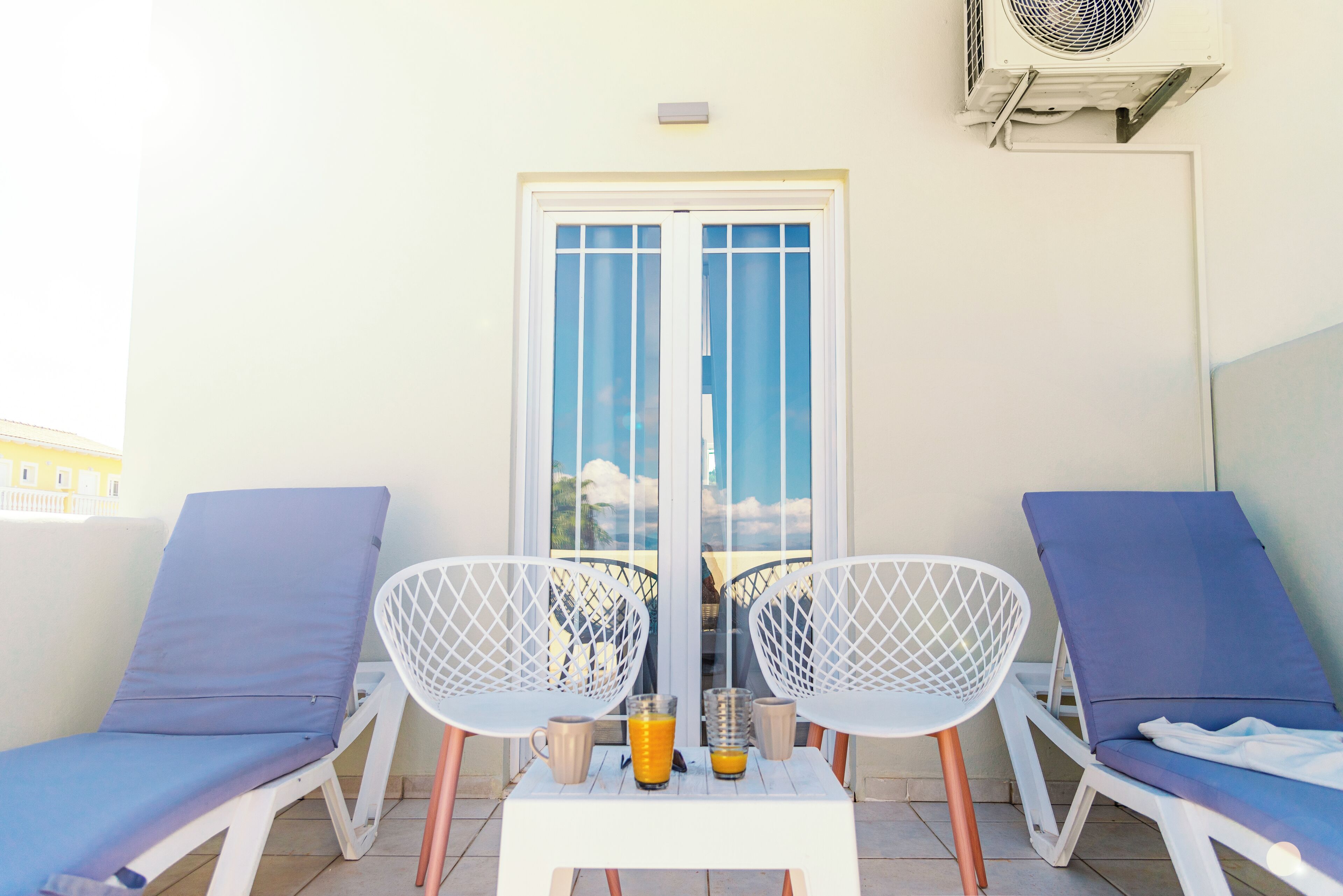 A balcony with two lounge chairs, a small table, and a glass of orange juice.