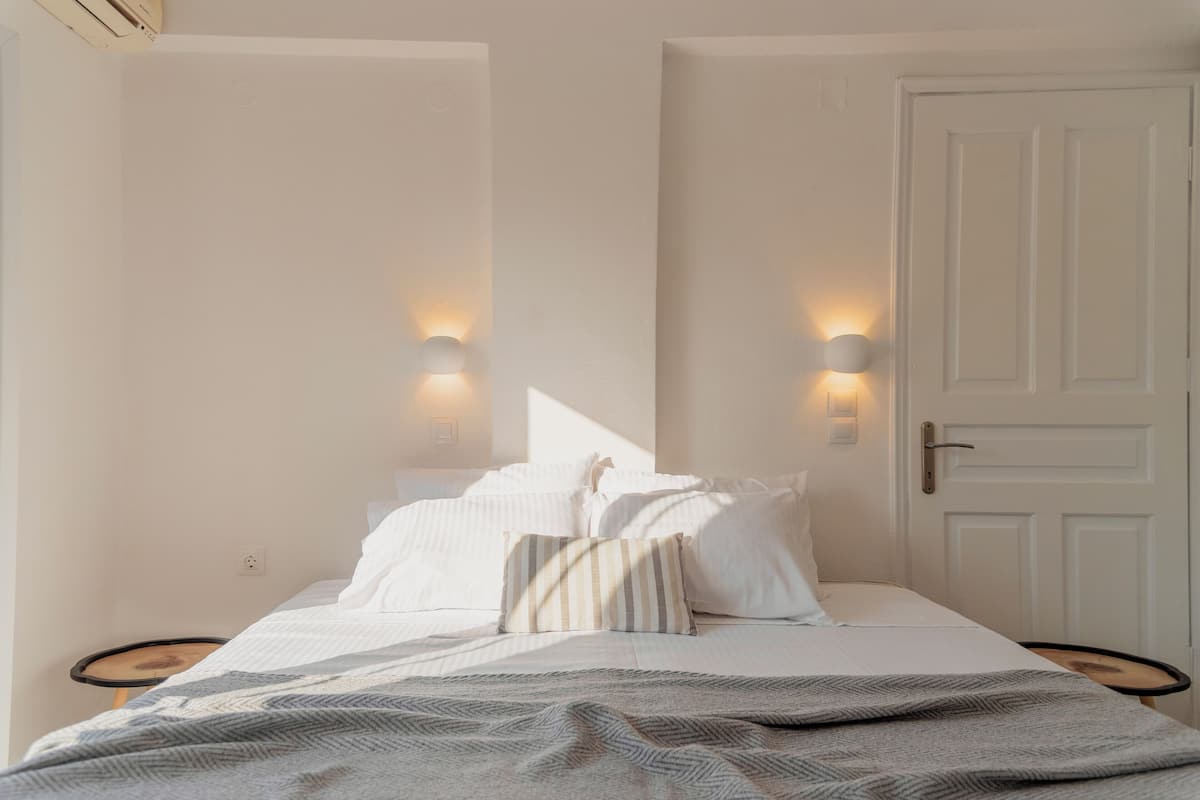 A neatly made bed with pillows and a blanket, two bedside tables, a door, and wall-mounted lights.