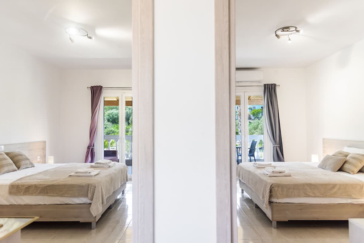A modern hotel room with a large bed, a balcony with curtains, and a view of greenery.