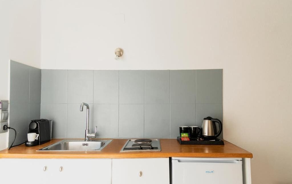 A kitchen with a sink, a coffee maker, a kettle, and a compact refrigerator.