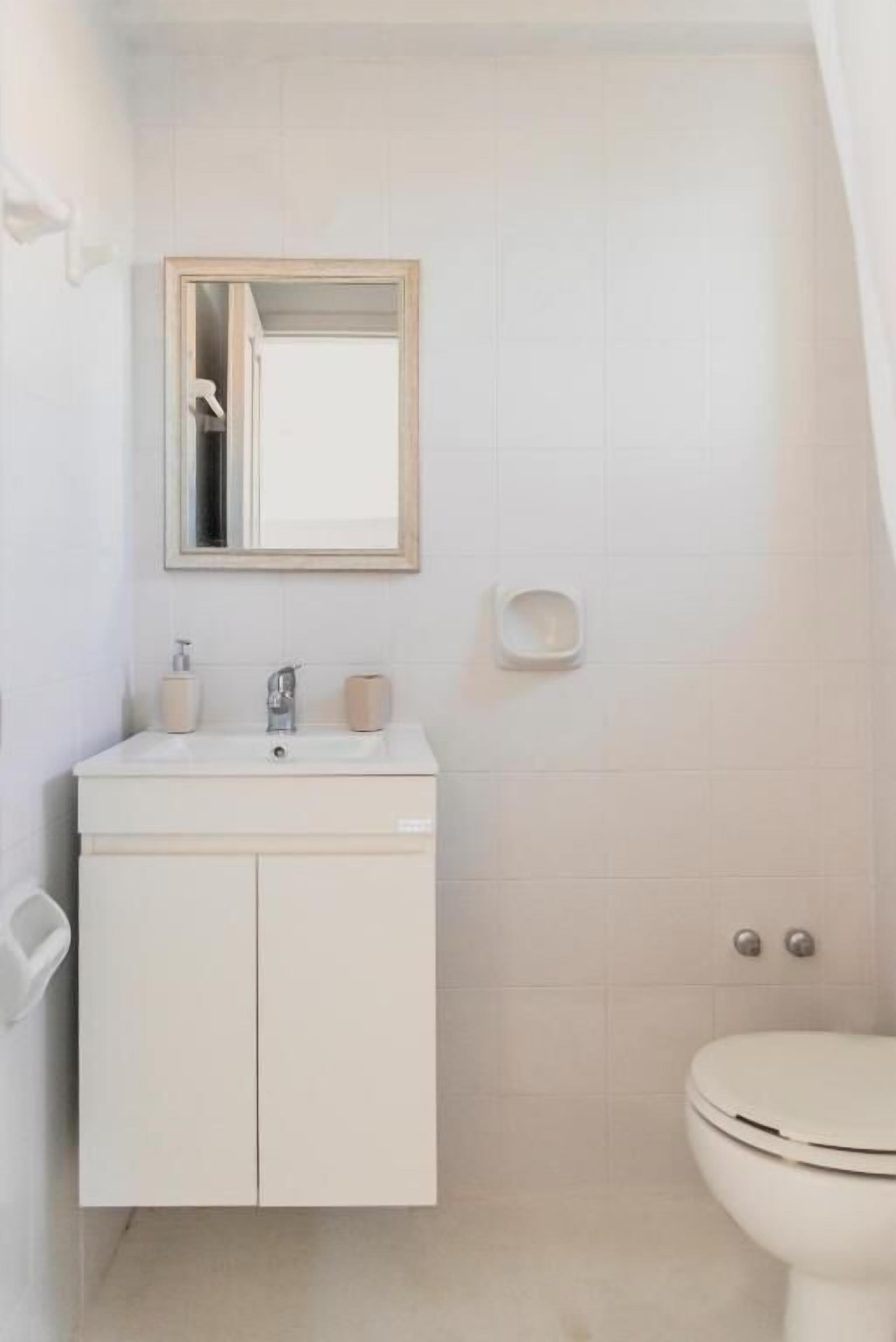 Un baño con lavamanos, espejo e inodoro blancos.