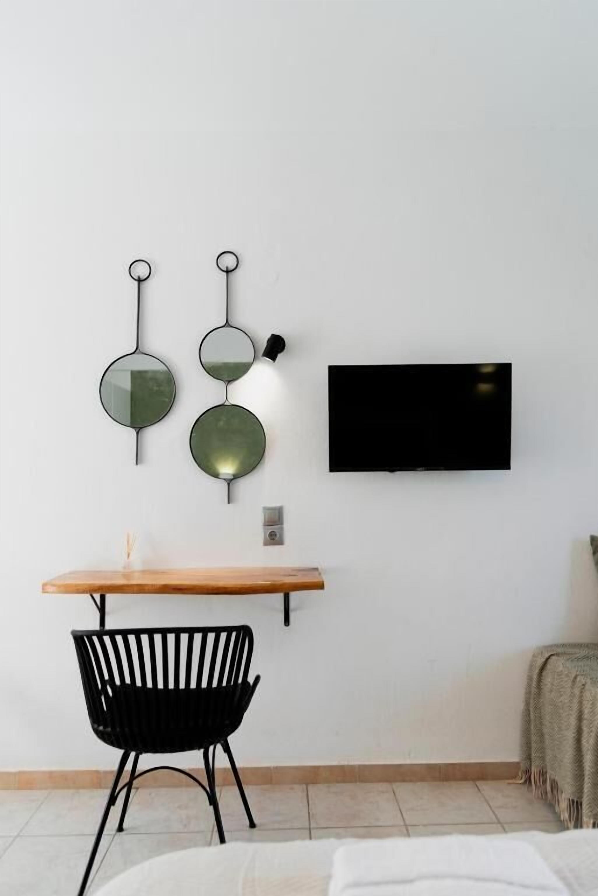 A modern room with a flat-screen TV, a wooden desk, a black chair, and wall-mounted mirrors.
