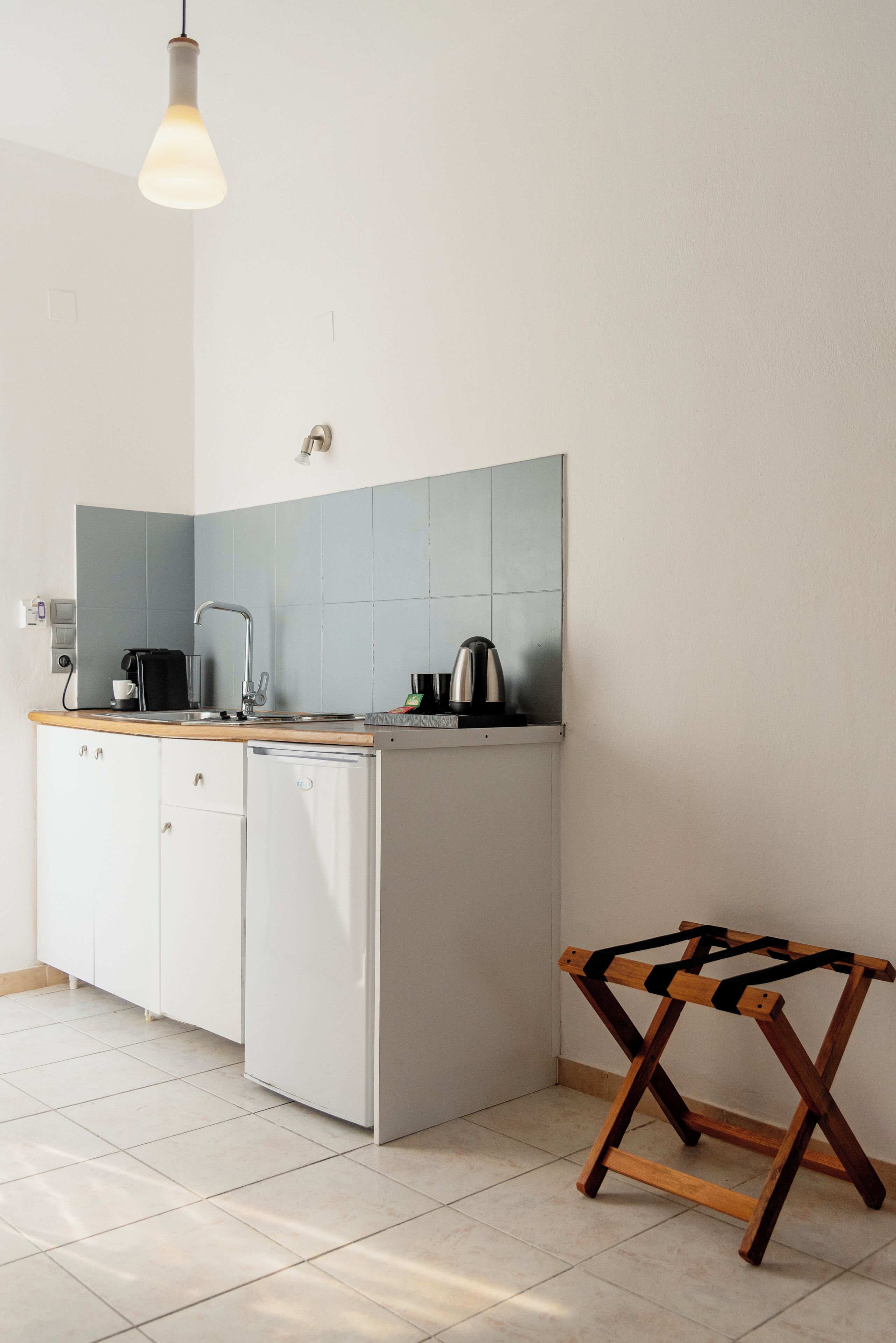 Cocina compacta con un lavamanos, cafetera, hervidor y refrigerador pequeño.