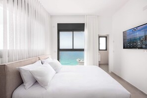 Habitació d'hotel amb llit, televisió penjada a la paret i vista al mar.