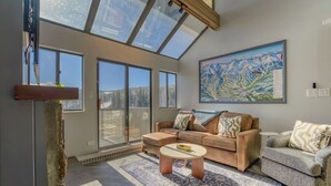Ein geräumiges Wohnzimmer mit großem Fenster, einer Sofagarnitur, einem Couchtisch und einem Gemälde an der Wand.