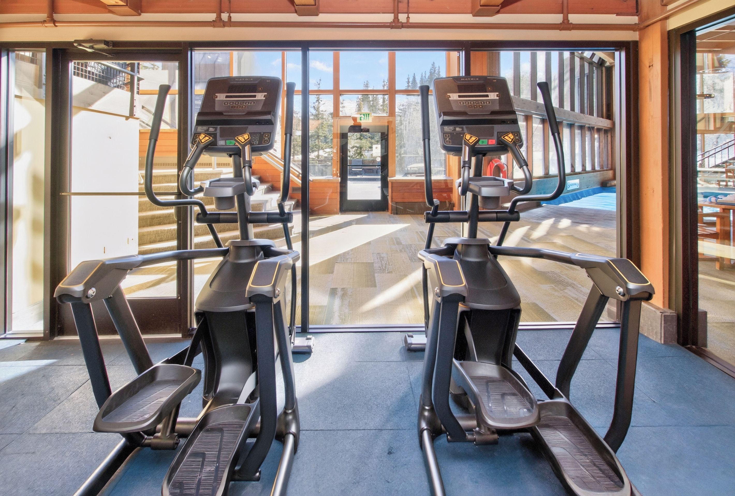 A gym with two treadmills facing a large window with a view of a pool and outdoor area.